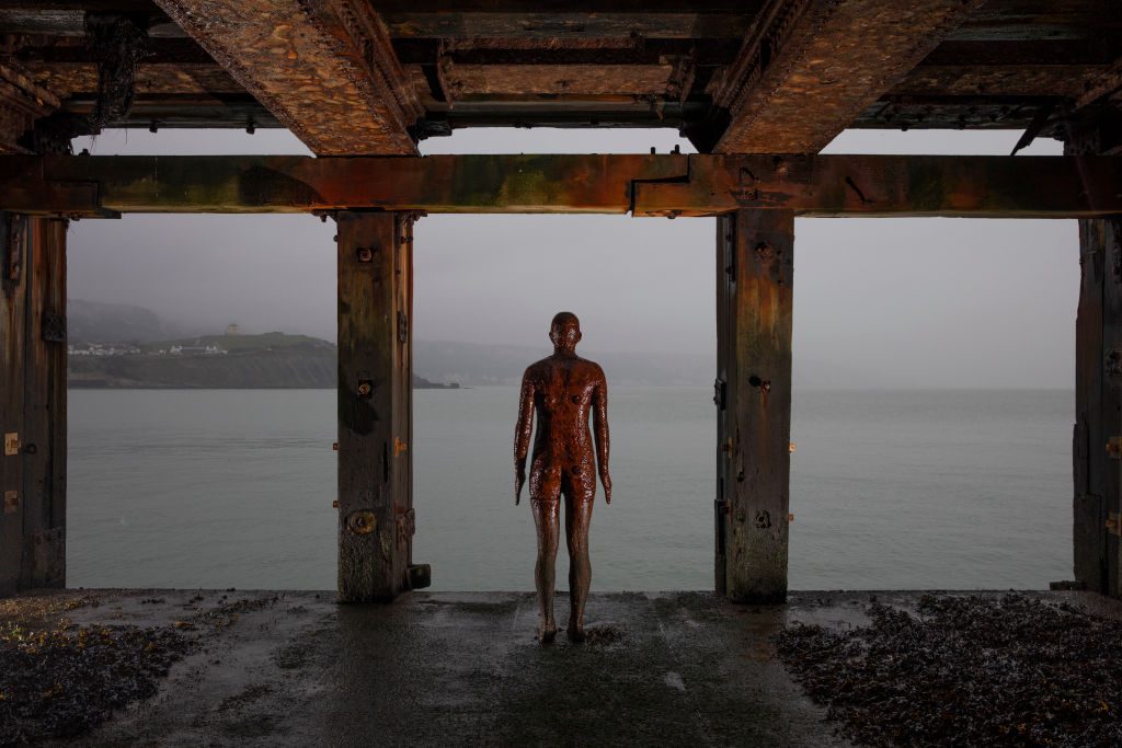 A sculpture by British artist Antony Gormley stands under the harbor wall on January 13, 2021 in Folkestone, United Kingdom. Photo by Dan Kitwood/Getty Images.