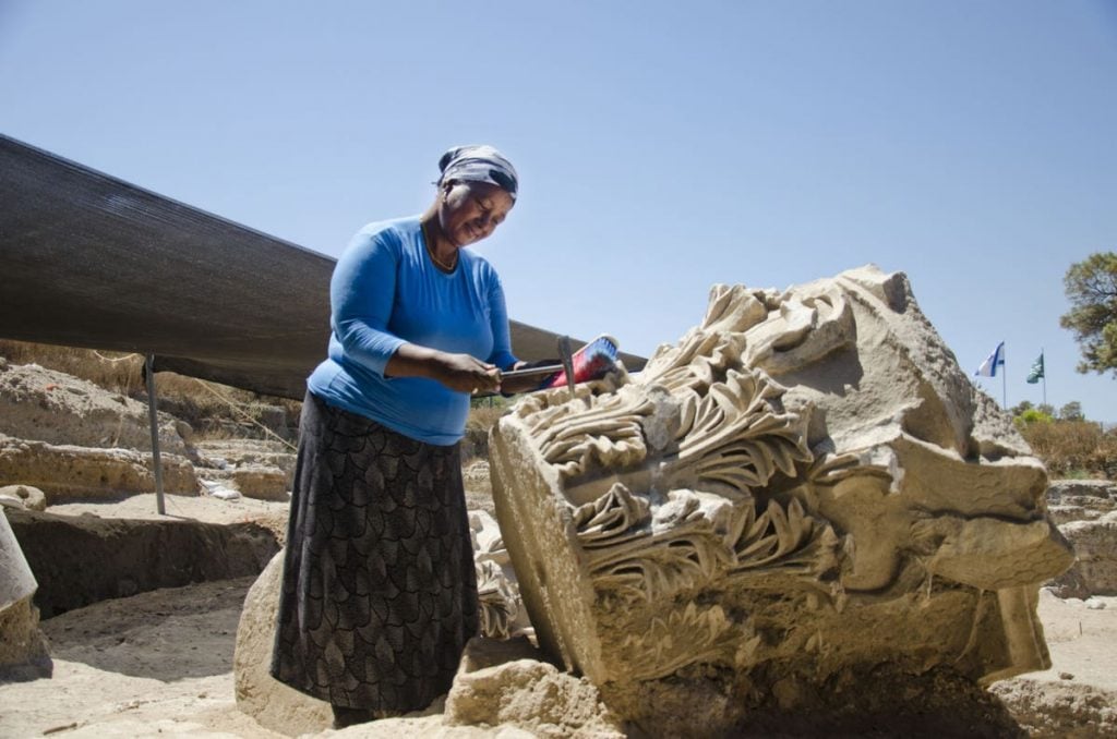 A woman stands next to a giant capital at the at the Roman basilica in Tel Ashkelon National Park. Photo by Yoli Shwartz courtesy of the Israel Antiquities Authority.