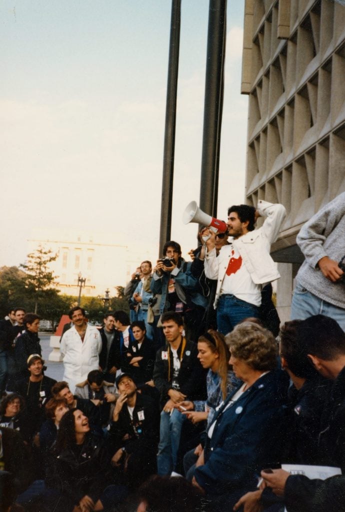 Gregg Bordowitz with a megaphone addressing a crowd of protestors in front of the Food and Drug Administration in 1988. Several people are laughing in the picture, and a sense of humor—one that's sometimes warped—hovers over his MoMA PS1 retrospective. Courtesy the artist.