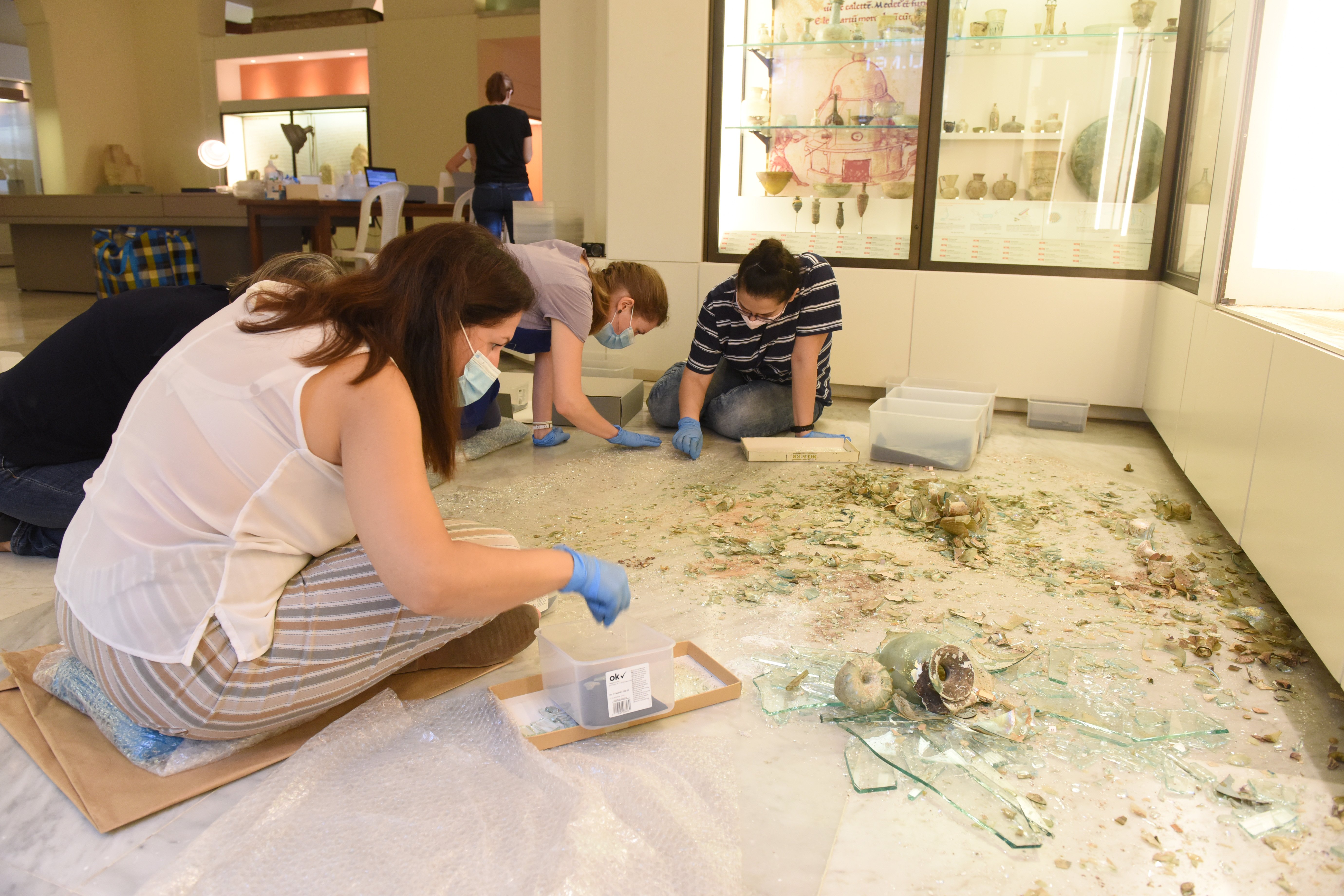 Conservators and student volunteers retrieve fragments of broken glass vessels from amongst the shattered glass from the display case and nearby windows at the Archaeological Museum, AUB. Courtesy of the AUB Office of Communications and Archaeological Museum.