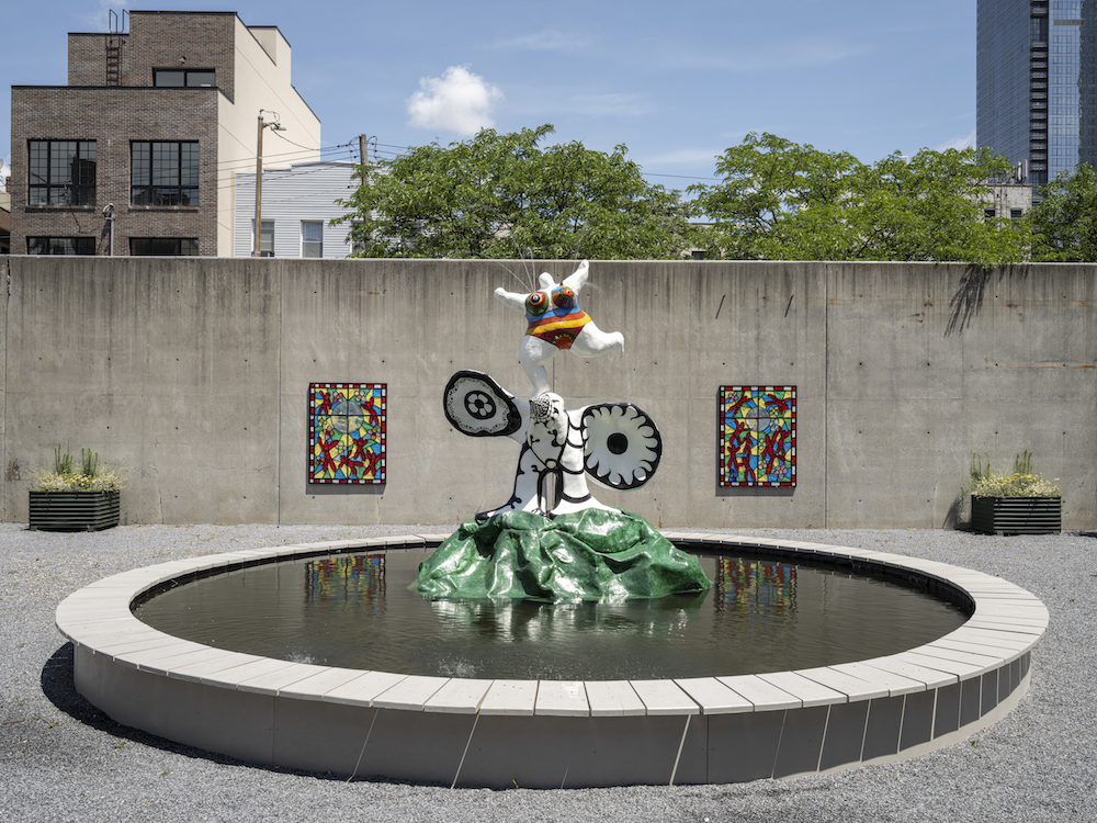 View of Niki de Saint Phalle La femme et L’oiseau fontaine (1967–88) and Raúl de Nieves The Stories of the Past Rejoice through Children’s Skies (2021) on view at MoMA PS1, New York. Image courtesy MoMA PS1. Photo: Kris Graves.