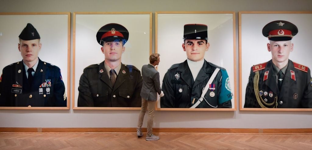 An employee of Grisebach auction house hangs giant photos by photographer Frank Thiel of the Allied soldiers who once patrolled Berlin that have been displayed at Checkpoint Charlie ar up for auction in Berlin on November 20, 2019. Photo by Tobias Schwarz/AFP via Getty Images.