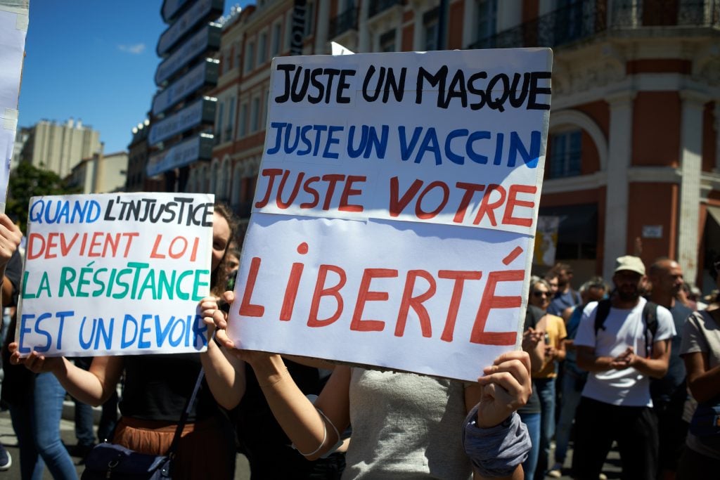 A protester holds a placard reading "Just a protective mask, just a jab, just your freedom." Thousands of people protested in Toulouse and elsewhere in France against the against the nation's health pass, which will be mandatory for going in public places such as cafes, theaters, concerts hall, shops, and public transportation. Photo by Alain Pitton/NurPhoto via Getty Images.