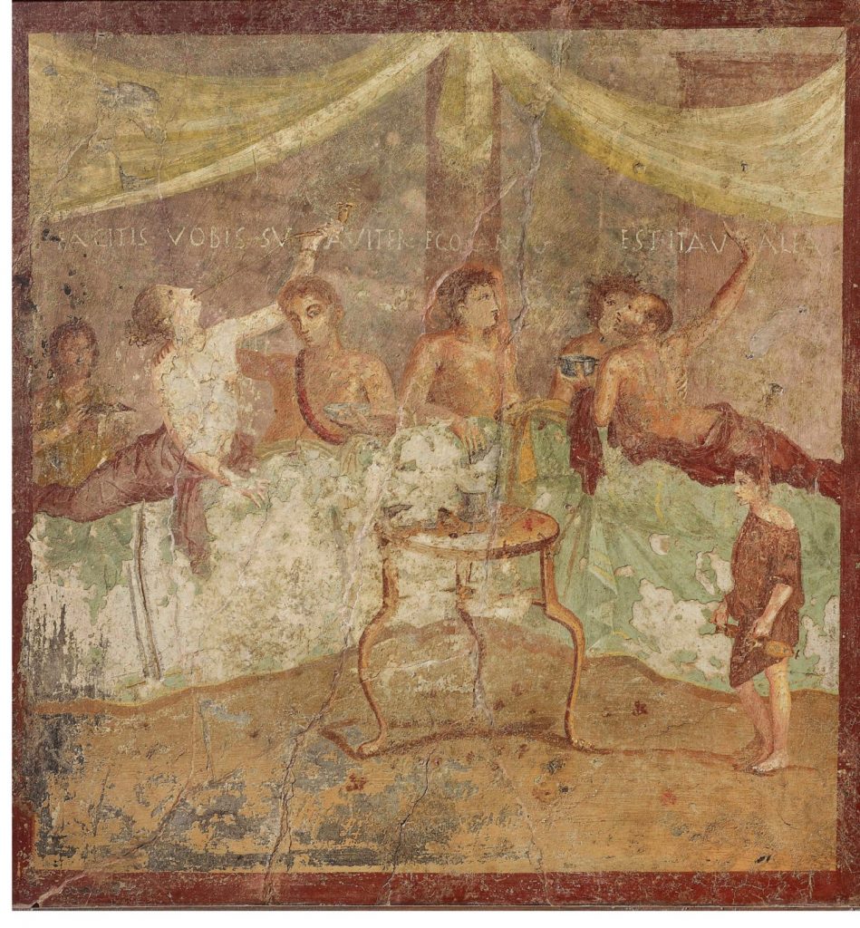Fresco from Pompeii showing a convivium, or banquet (AD 50–79). In the Latin caption, a woman offers to sing, and a man replies “Yes, you go for it!” Photo courtesy of the Museo Archeologico Nazionale di Napoli.