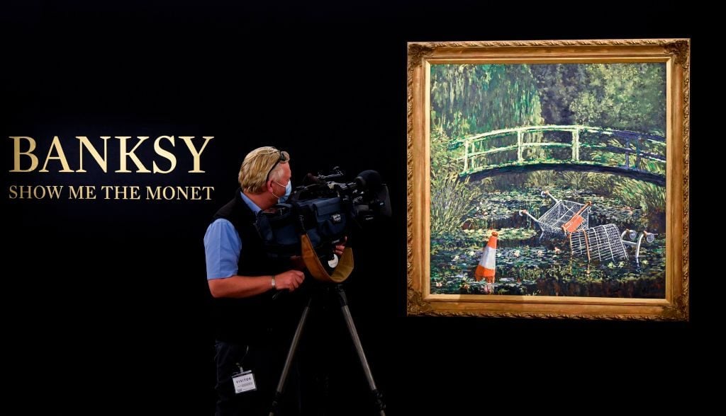 A television camera operator films an artwork entitled Show me the Monet by the artist Banksy during a photocall at Sotheby's.(Photo by DANIEL LEAL-OLIVAS / AFP)