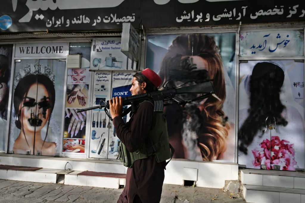 A Taliban fighter walks past a beauty salon with images of women defaced using spray paint in Shar-e-Naw in Kabul on August 18, 2021. (Photo by WAKIL KOHSAR/AFP via Getty Images)