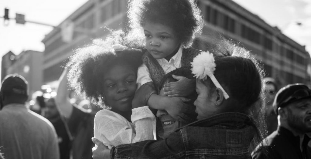 Devin Allen, <em>Untitled</em> (2015). Two daughters and a son hug their father during a protest against the police killing of Freddie Gray in Baltimore, Maryland. Collection of the Smithsonian National Museum of African American History and Culture, gift of Devin Allen, ©Devin Allen.