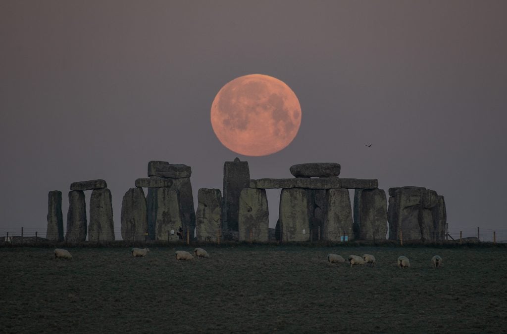 The full moon sets behind Stonehenge on April 27, 2021 in Amesbury, England. Photo by Finnbarr Webster/Getty Images.