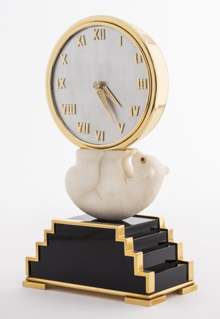 Gold clock set with neo-Art Deco gemstones, 18k gold case with diamonds, embellished gold hands nestled in the straight legs of an elongated bear with ruby â€‹â€‹eyes outlined in gold.