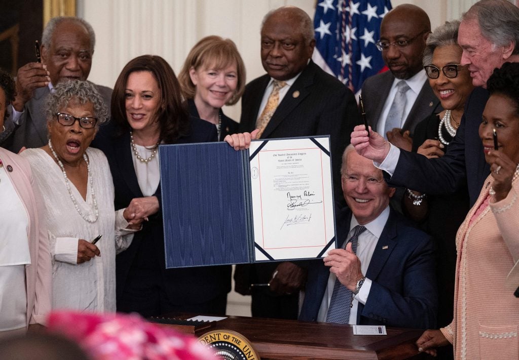 US Vice President Kamala Harris and Opal Lee (2nd L), the activist known as the Grandmother of Juneteenth, watch as President Joe Biden holds the signed Juneteenth National Independence Day Act, in the East Room of the White House, June 17, 2021, in Washington. Photo by Jim Watson/AFP via Getty Images.