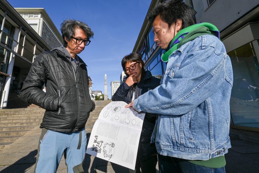 Left to right: Iswanto Hartono, Daniella Fitriap and Reza Afisina from the artist collective ruangrupa in front of the ruruHaus in the October issue of <em>Asphalt</em> with the complete artist list of the exhibiting artists of documenta. (Photo by Uwe Zucchi/picture alliance via Getty Images)