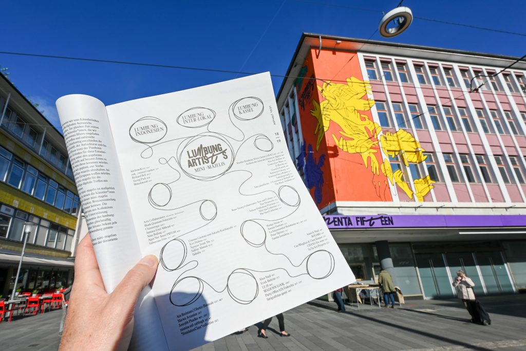 The October issue of the street newspaper <em>Asphalt</em>, opened to the page with the complete artist list of the exhibiting artists of documenta 15. (Photo by Uwe Zucchi/picture alliance via Getty Images)