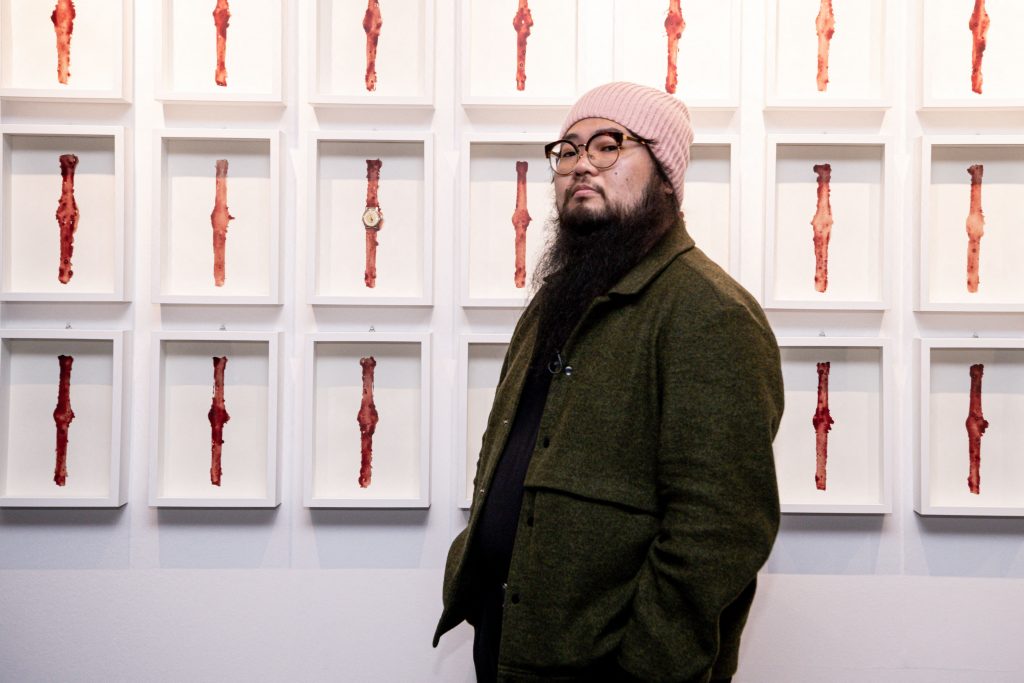 Chinese dissident artist Badiucao poses next to his artwork entitled "Watch, 2021" on November 12, 2021 at the exhibition "China is (not) near -- works of a dissident artist", opening at the Santa Giulia museum in Brescia, Lombardy. Photo by Piero Cruciatti/AFP via Getty Images.