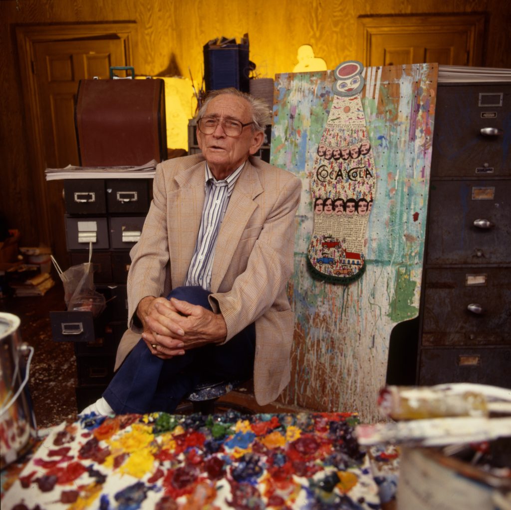 Portrait of American artist and minister Howard Finster as he poses in his studio, with one of his paintings behind him, 1990s. Photograph by Anthony Barboza/Getty Images.