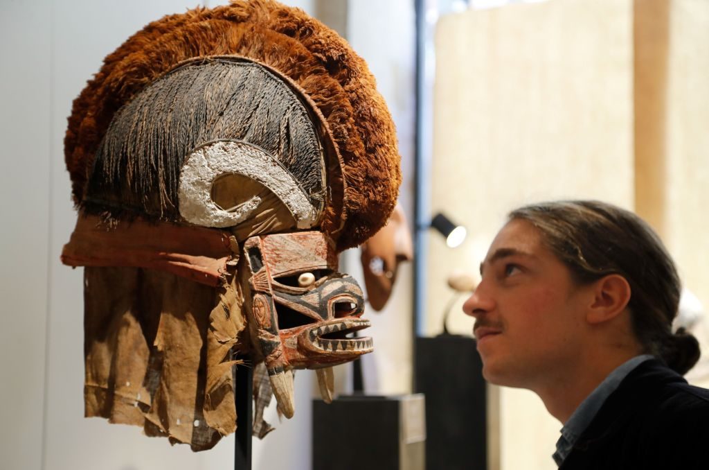 A man looks at a Tatanua mask from New Ireland, in Papua New Guinea, and dated of end of the 19th century. Photo by François Guillot/AFP via Getty Images.