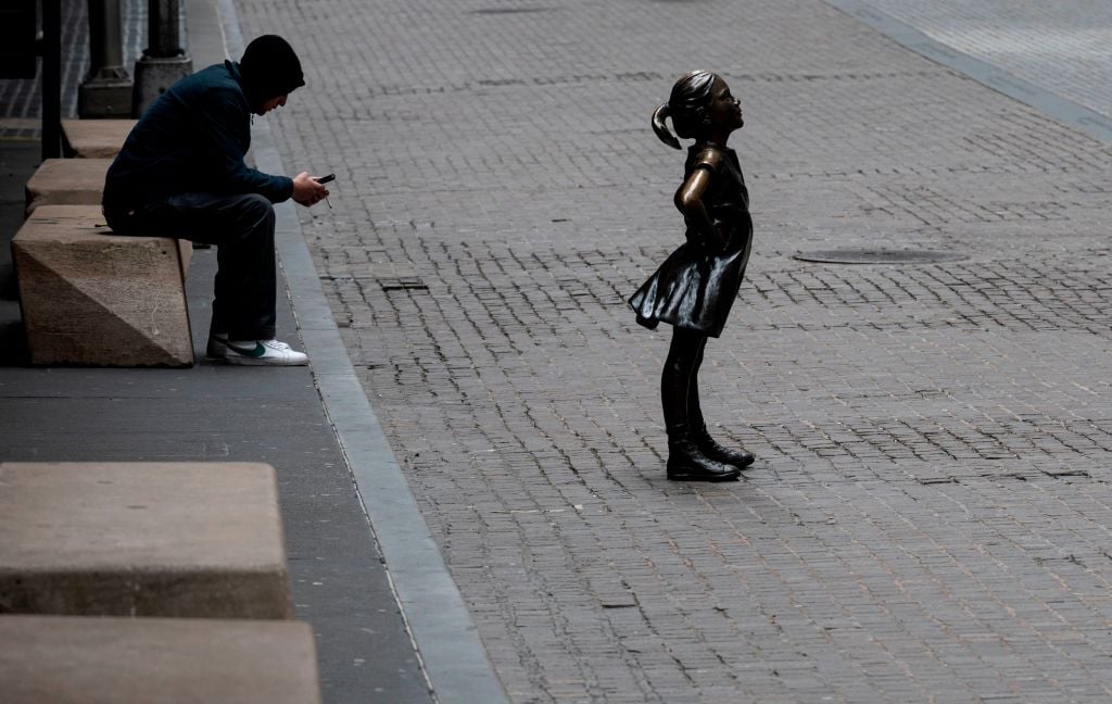 A man sits next to the fearless girl statue next to the New York Stock Exchange (NYSE) on April 20, 2020 at Wall Street in New York City. Photo: Johannes Eisele / AFP via Getty Images.