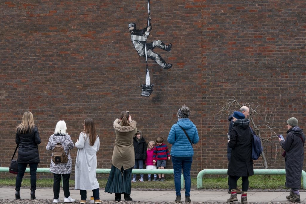 Members of the public take pictures of a Banksy miral on the side of HMP Reading on March 5, 2021 in Reading, England. (Photo by Ming Yeung/Getty Images)