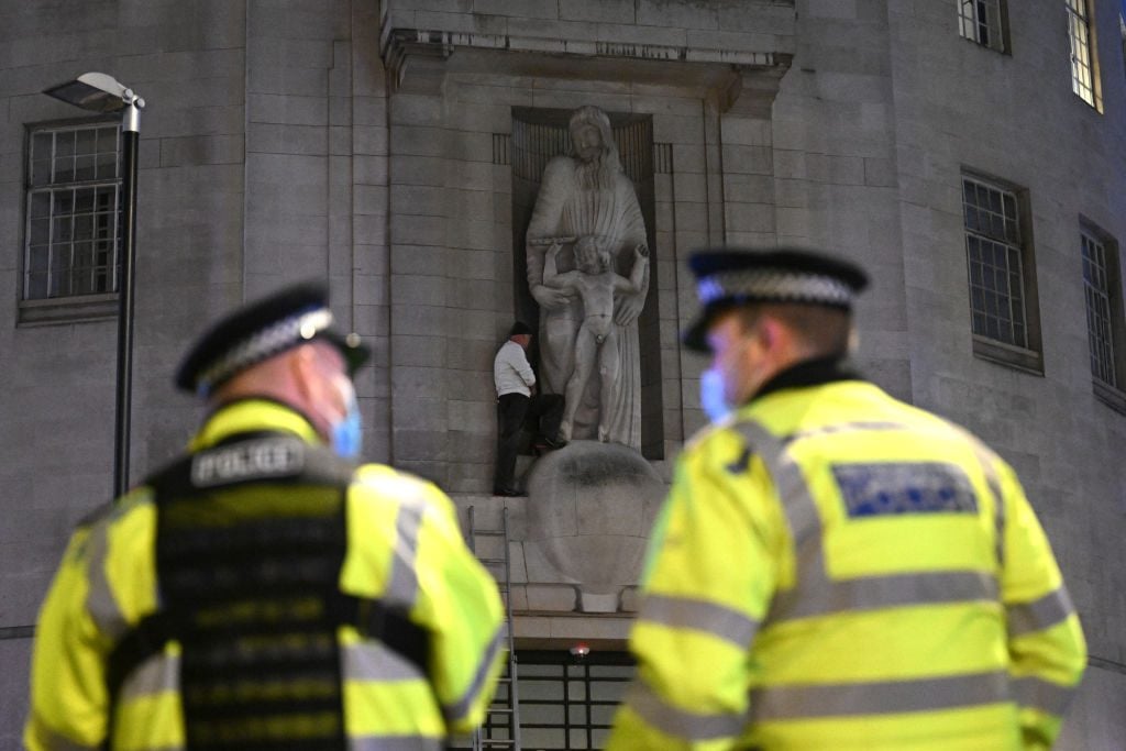 Police officers look on as a protester attempts to damage a statue by sculptor Eric Gill at the BBC Broadcasting House on January 12, 2022 in London. (Photo by Leon Neal/Getty Images)