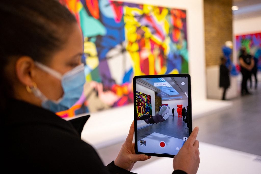 A member of a staff uses the Acute Art app to display an (AR) augmented reality artwork entitled COMPANION (EXPANDED) by American artist KAWS, during a press preview for the exhibition 'KAWS: NEW FICTION' at the Serpentine North gallery in London on January 18, 2022. - RESTRICTED TO EDITORIAL USE - MANDATORY MENTION OF THE ARTIST UPON PUBLICATION - TO ILLUSTRATE THE EVENT AS SPECIFIED IN THE CAPTION (Photo by Tolga Akmen / AFP) / RESTRICTED TO EDITORIAL USE - MANDATORY MENTION OF THE ARTIST UPON PUBLICATION - TO ILLUSTRATE THE EVENT AS SPECIFIED IN THE CAPTION / RESTRICTED TO EDITORIAL USE - MANDATORY MENTION OF THE ARTIST UPON PUBLICATION - TO ILLUSTRATE THE EVENT AS SPECIFIED IN THE CAPTION (Photo by TOLGA AKMEN/AFP via Getty Images)
