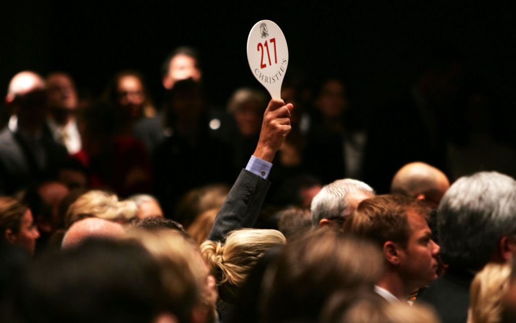 A man holds his hand up while bidding on a work of art inside the auction house Christie's. Photo by Spencer Platt/Getty Images.