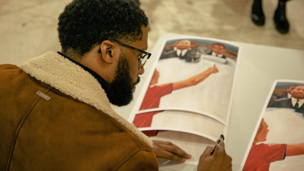 Jonathan Harris signing copies of his painting <em>Critical Race Theory</em> (2021). Photo courtesy of Jonathan Harris. 