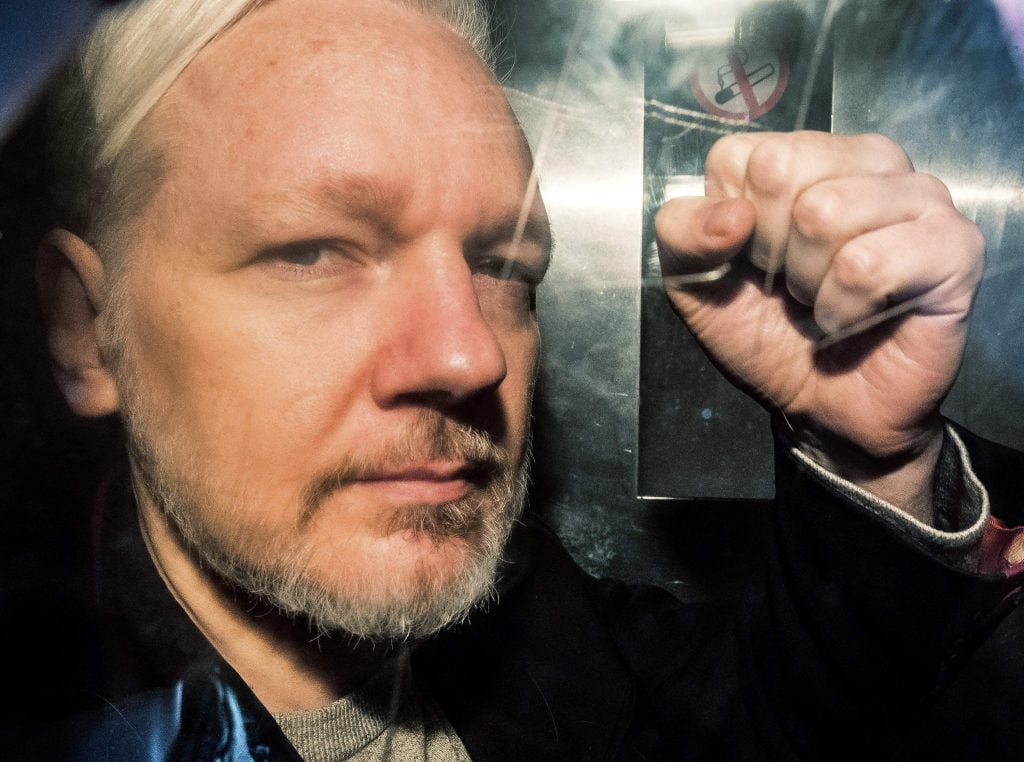 WikiLeaks founder Julian Assange gestures from the window of a prison van as he is driven into Southwark Crown Court in London on May 1, 2019, before being sentenced to 50 weeks in prison for breaching his bail conditions in 2012. - A British judge on Wednesday sentenced WikiLeaks founder Julian Assange to 50 weeks in prison for breaching his bail conditions in 2012. Assange took refuge in Ecuador's London embassy to avoid extradition to Sweden and was only arrested last month after Ecuador withdrew his asylum status. (Photo by Daniel LEAL / AFP) (Photo by DANIEL LEAL/AFP via Getty Images)
