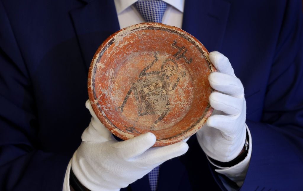 A politician presents a clay bowl from the Mexican Mayan culture that was among 13 arteficts from the Central American culture, which the police had unearthed in the cellar of a house in the Altmark region. Photo by Ronny Hartmann/picture alliance via Getty Images.