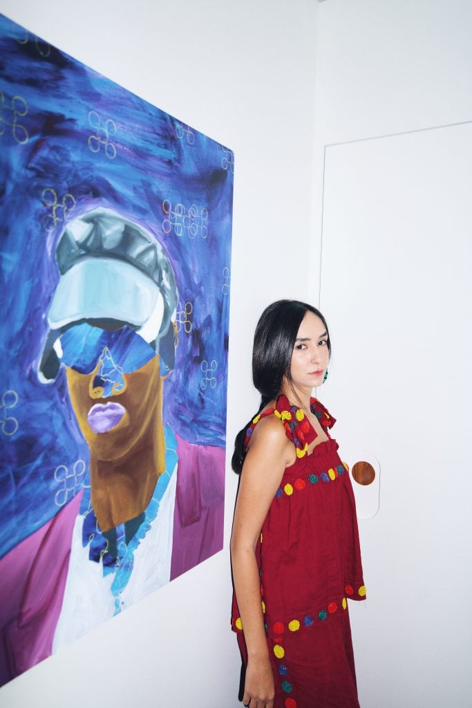Jessica with a painting by O bastardo from the series "Pretos de Griffe" (2021). Courtesy Jéssica Cinel.