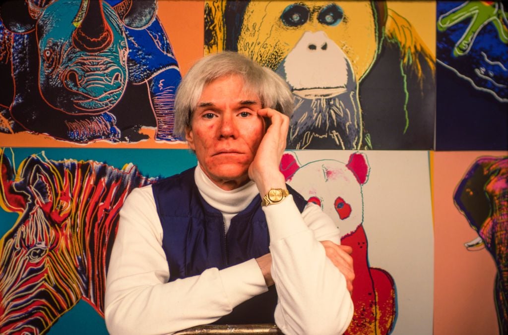 American Pop artist Andy Warhol (1928 - 1987) sits in front of several paintings in his 'Endangered Species' at his studio, the Factory, in Union Square, New York, New York, April 12, 1983. Photo by Brownie Harris/Corbis via Getty Images.