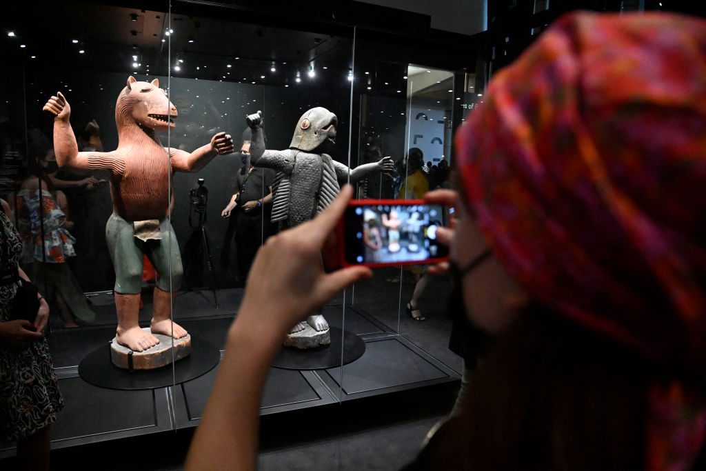 A woman photographs anthropo-zoomorphic statues depicting King Glele (L)and King Behanzin (R) during an exhibition of returned looted Benin artefacts and exhibition of contemoprary artworks at the presidency in Benin's capital Cotonou, on February 18, 2022. Photo by PIUS UTOMI EKPEI/AFP via Getty Images.