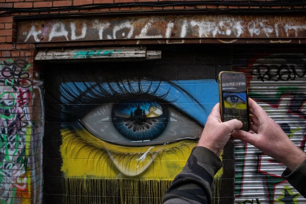 A resident takes a photograph of a new mural in Cardiff depicting Ukraine's capital under siege on March 1, 2022 in Cardiff, Wales. (Photo by Huw Fairclough/Getty Images)