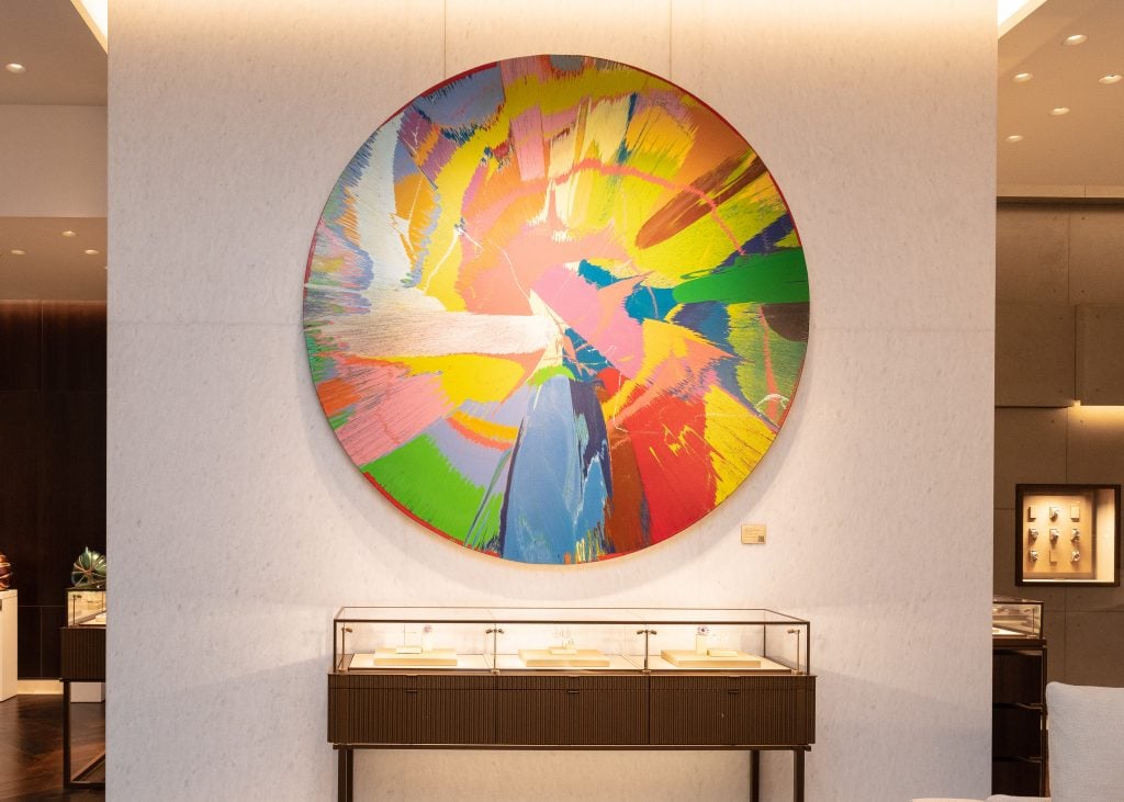 Damien Hirst's <em>Beautiful, red, edgy, comet, purple, spunk painting</em> hangs above a jewelry display. Photo: Hannah Turner Harts/BFA. Courtesy of Bucherer.