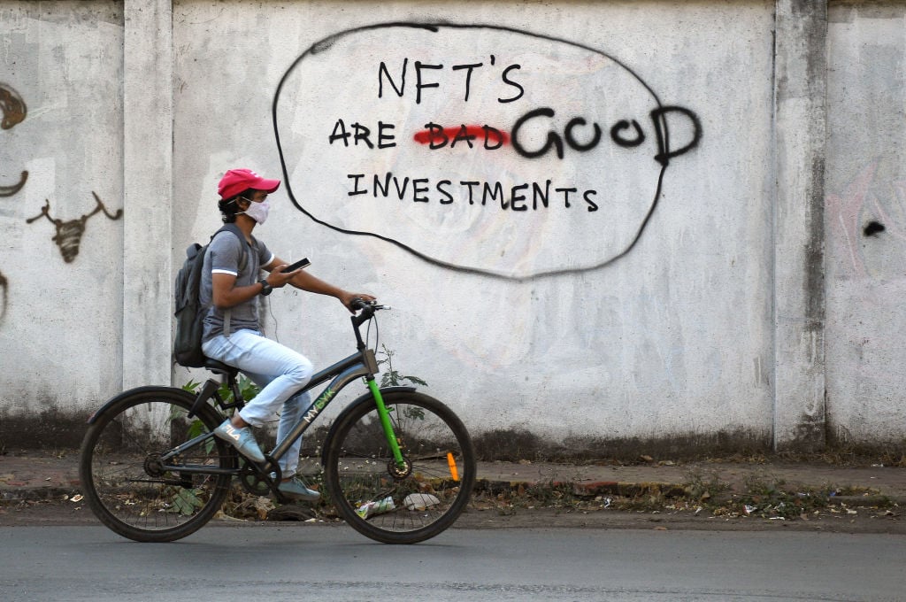 A man rides a bicycle past a graffiti a wall that reads "NFT's are good investments" in Mumbai. (Photo by Ashish Vaishnav/SOPA Images/LightRocket via Getty Images)