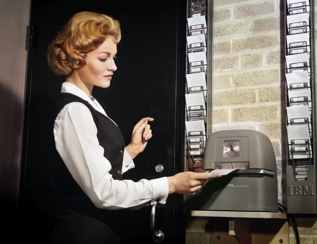 A woman punching a time clock at work, ca. 1960s