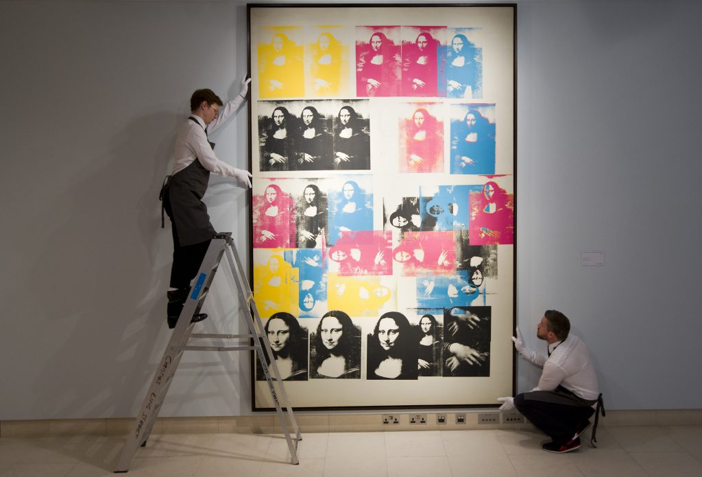 Employees of Christie's with Andy Warhol's <i>Colored Mona Lisa</i> (1963). (Photo by Justin TALLIS / AFP) (Photo by JUSTIN TALLIS/AFP via Getty Images)