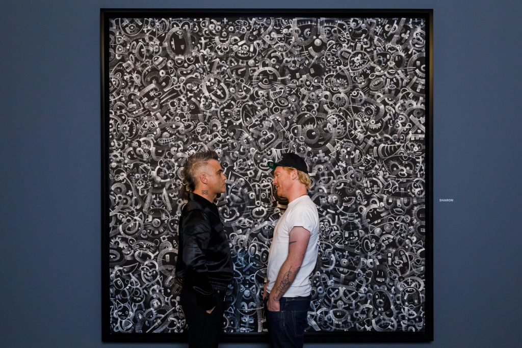 Robbie Williams (left) and Ed Godrich posing in front of their painting Sharon at their debut exhibition 'Black and White Paintings' at Sotheby's London. Courtesy Sotheby's.