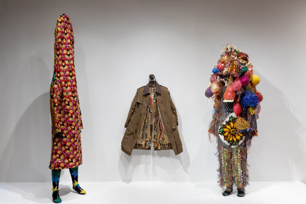 Three works by Nick Cave, (left) Soundsuit (2018), (center) Hustle Coat (2017) and (right) Soundsuit (2006).  Photo by Jenna Bascom.  Courtesy of the Museum of Arts and Design.