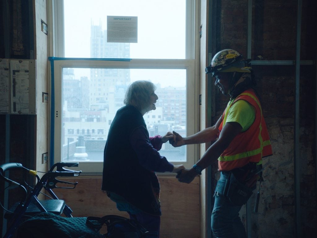 Merle Lister dances with a construction worker in <em>Dreaming Walls: Inside the Chelsea Hotel</em>, directed by Amélie van Elmbt and Maya Duverdier. Film still courtesy of Magnolia Pictures, ©Clindoeilfilms. 