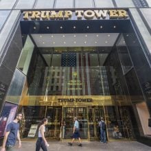 Entrance of Trump Tower in New York City with pedestrians walking by and reflections on the glass facade.