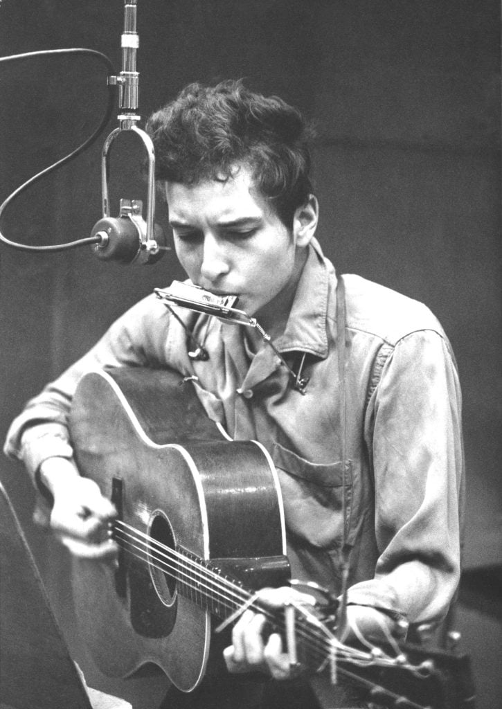 Bob Dylan recording with an acoustic Gibson guitar and a harmonica in 1961 at Columbia Studio in New York City, New York. Photo by Michael Ochs Archives/Getty Images.