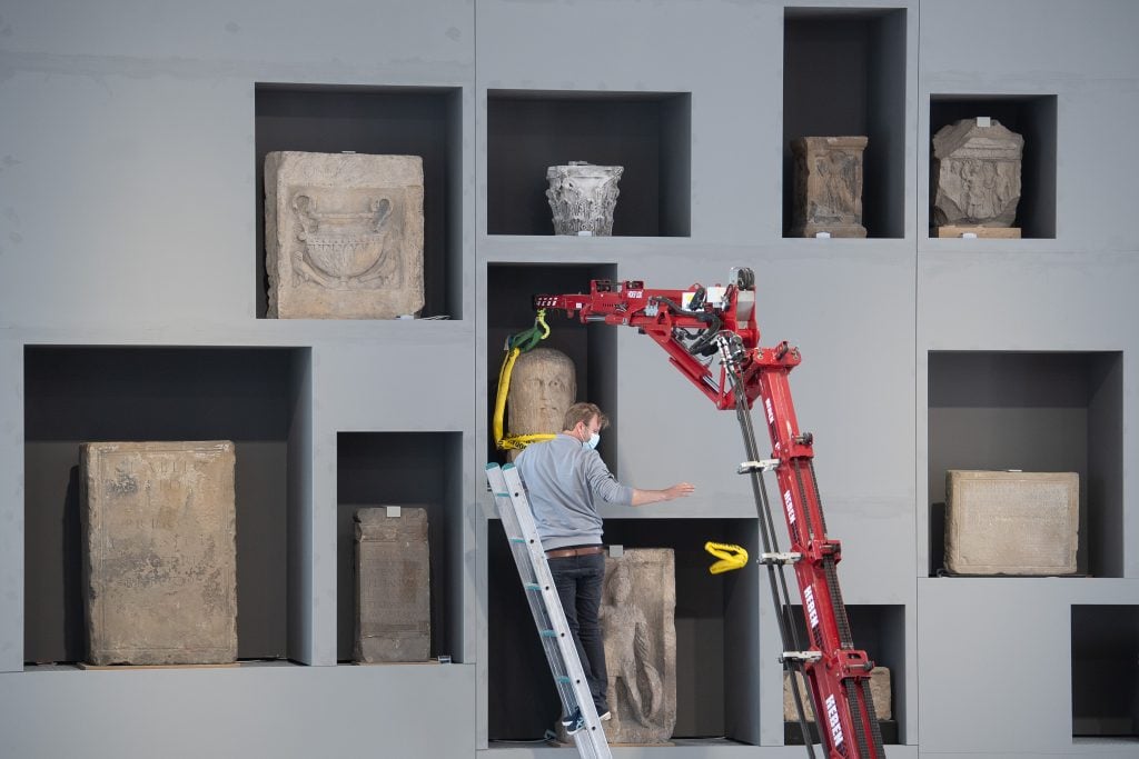 An art-logistics expert secures a stone's placement on a shelf in the stone hall of the Landesmuseum Mainz. (Photo by Sebastian Gollnow/picture alliance via Getty Images)