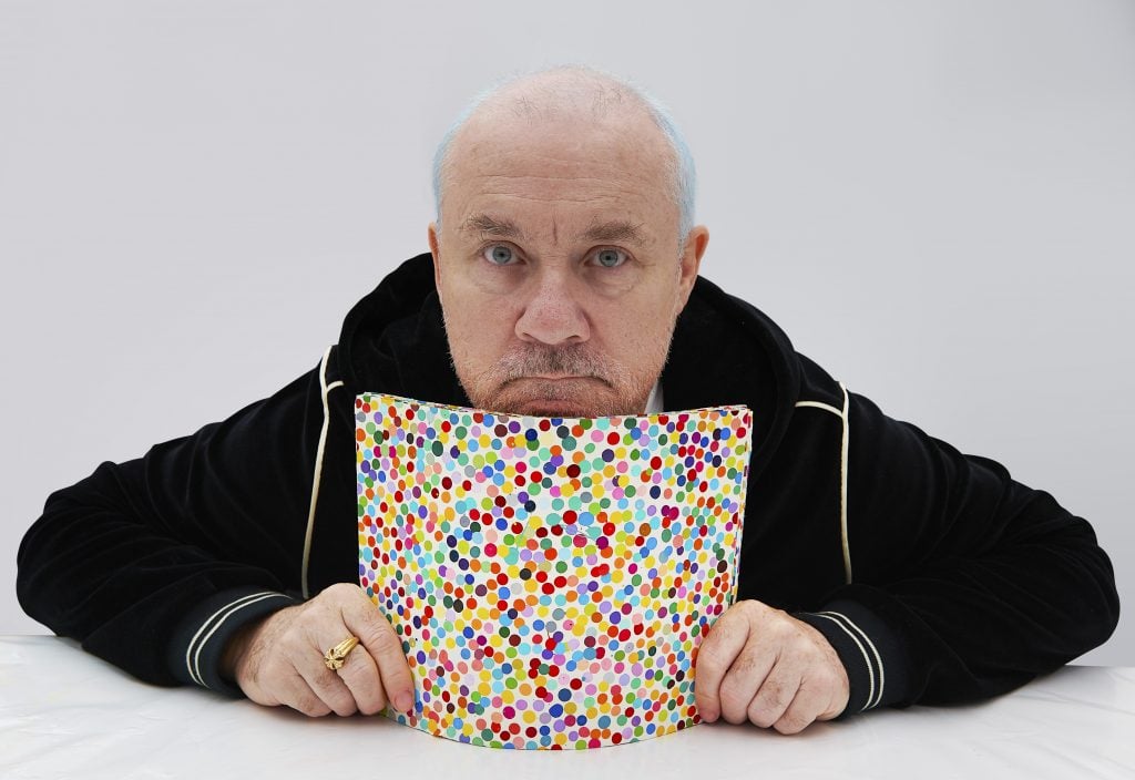 Damien Hirst with The Currency artwork, 2021. Photographed by Prudence Cuming Associates Ltd. © Damien Hirst and Science Ltd. All rights reserved, DACS 2022.