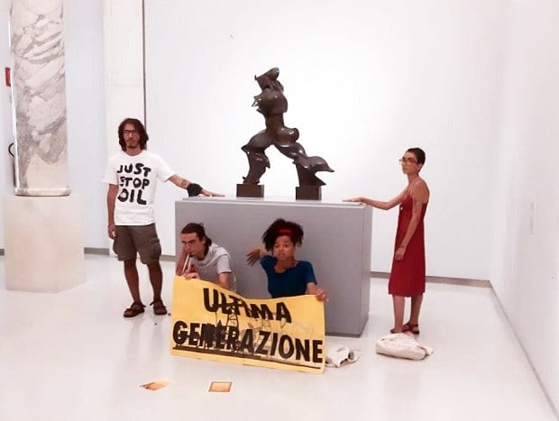Members of the activist group Ultima Generazione glued to a plinth supporting Boccioni’s 1913 bronze, <i>Unique Forms of Continuity in Space</i> at the Museo del Novecento in Milan on July 30. Photo courtesy of Ultima Generazione.