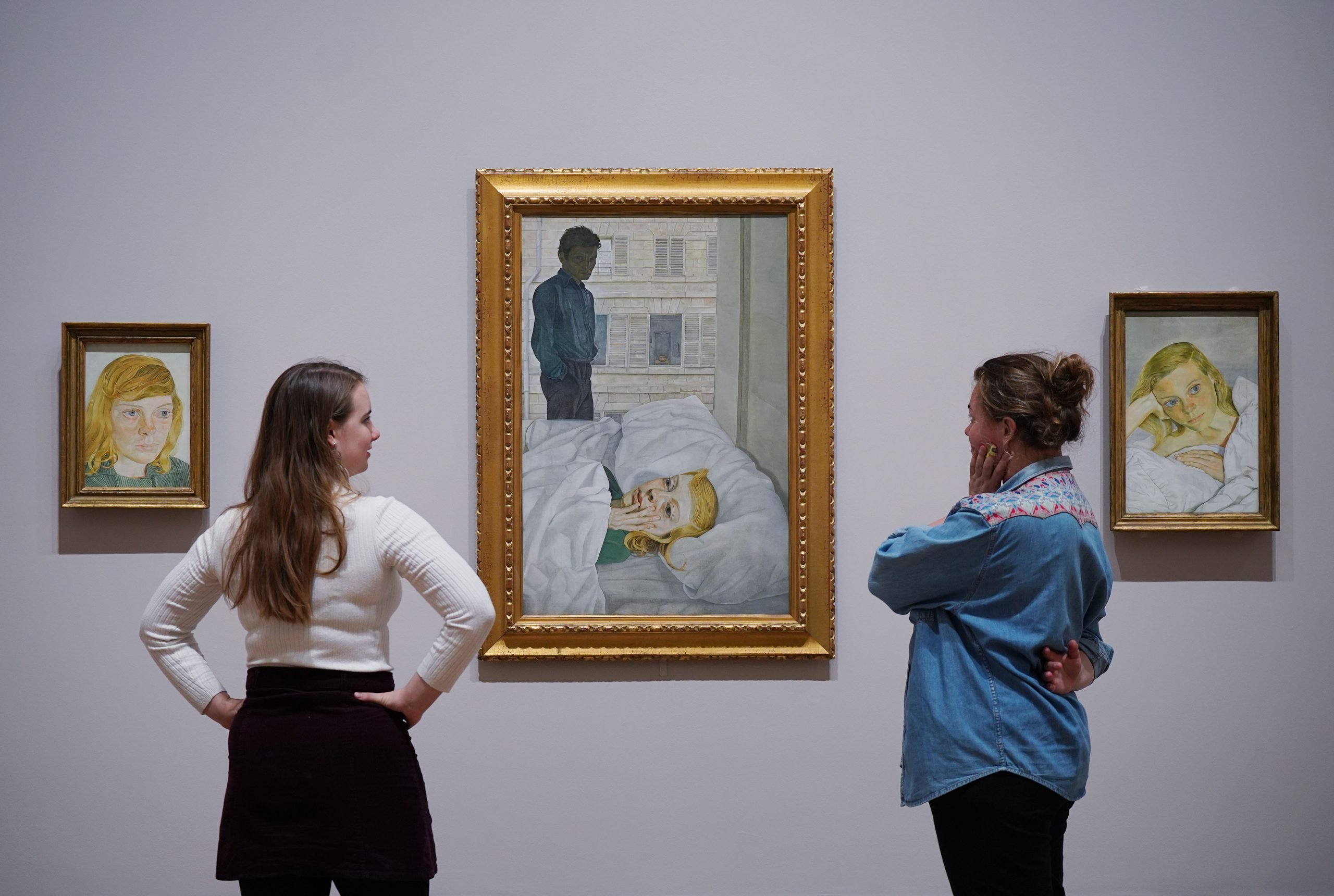 Gallery staff pose next to paintings by Lucian Freud (L-R) - Girl in a Green Dress (1954); Hotel Bedroom (1954), and Girl in Bed (1952)—on show at a photocall for the Credit Suisse exhibition: "Lucian Freud: New Perspectives" at the National Gallery in London. Photo by Yui Mok/PA Images via Getty Images.