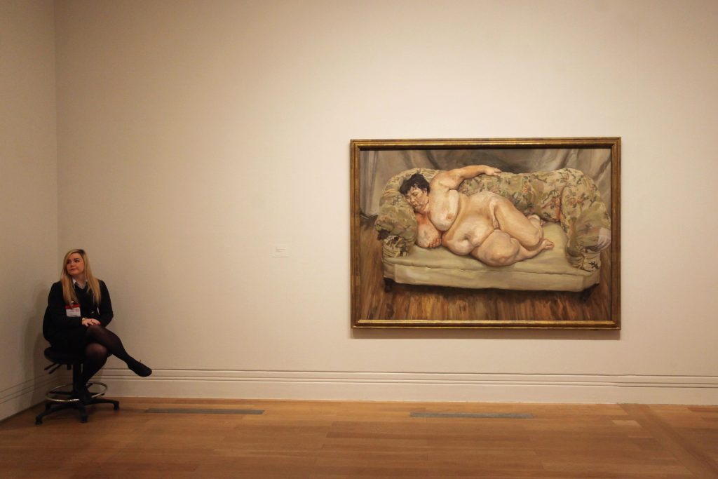 LONDON, ENGLAND - FEBRUARY 08: A gallery assistant sits next to the Lucian Freud painting 'Benefits Supervisor Sleeping' in the 'Lucian Freud Portraits' exhibition at the National Portrait Gallery on February 8, 2012 in London, England. The exhibition, which officially open to the general public on February 9, 2012, features 130 artworks spanning the length of Freud's painting career from the early 1940s until his final, unfinished work. (Photo by Oli Scarff/Getty Images)
