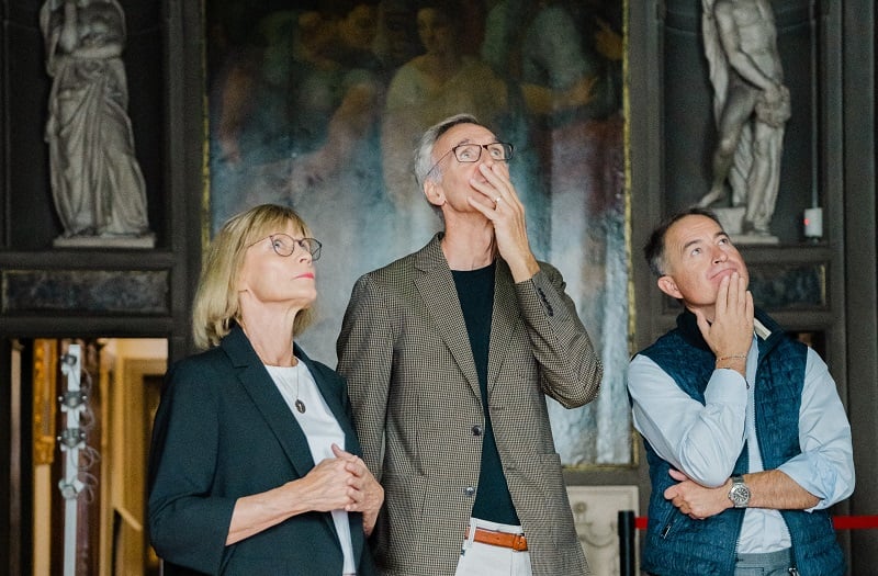 Project donors Margie MacKinnon, Wayne McArdle, and Christian Levett watch the descent of Artemisia Gentileschi, <em>Allegory of Inclination</em> (1816) from the ceiling of the Casa Buonarroti, Florence. Photo by Olga Makarova, courtesy of the Casa Buonarroti, Florence.