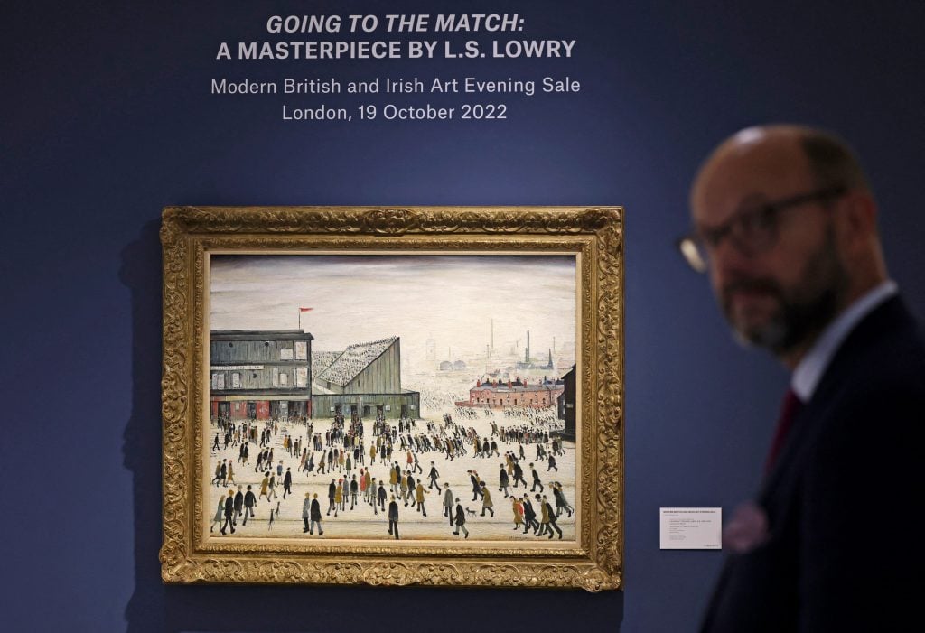 A visitor walks past L.S. Lowry's <em>Going to the Match</em>, on display at a Christie's exhibition in Dubai on September 15, 2022. Photo by Karim Sahib/AFP via Getty Images.