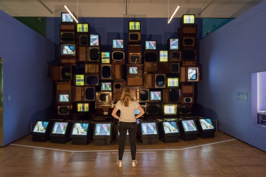 A staff member looks at Mirage Stage (1986) by Nam June Paik, a video sculpture featuring 33 TV monitors (copyright Nam June Paik Estate) in the exhibition 
