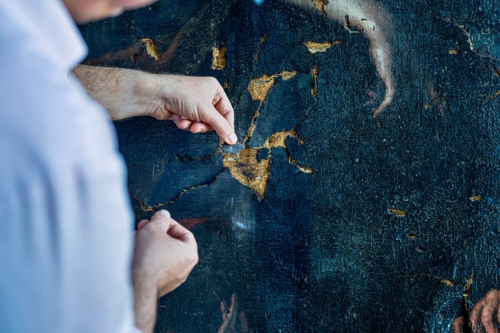 Ulrich Birkmaier attempts to match a paint fragment to losses in Artemisia Gentileschi's <em>Hercules and Omphale</eM> at the J Paul Getty Museum in Los Angeles. Photo by Cassia Davis, ©2022 J. Paul Getty Trust/Sursock Palace Collections, Beirut, Lebanon.