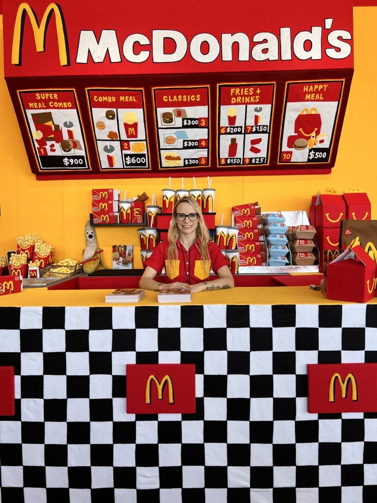 Lucy Sparrow behind the counter at her Mcdonald’s installation at Scope Miami Beach. Photo by Jo Brooks PR.